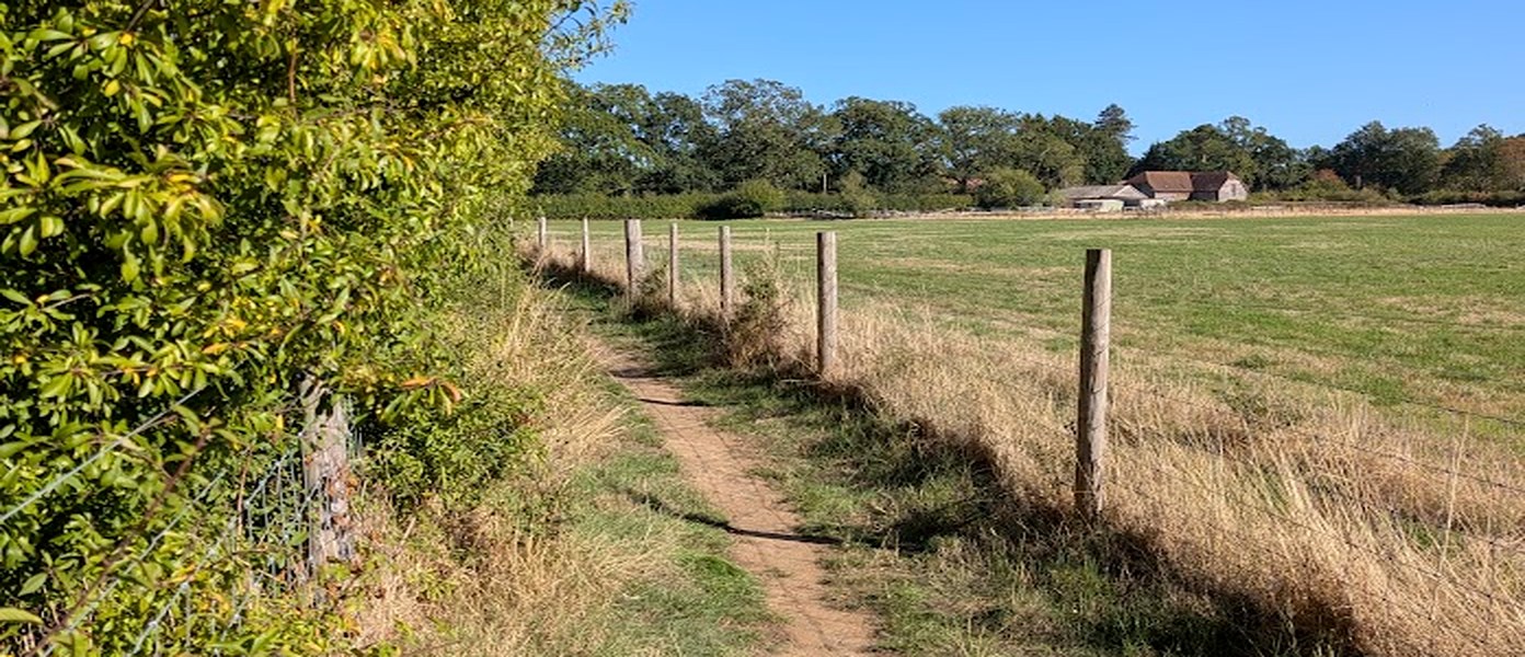 Church Path winding between a hedgerow and open fields, with a farmhouse in the distance